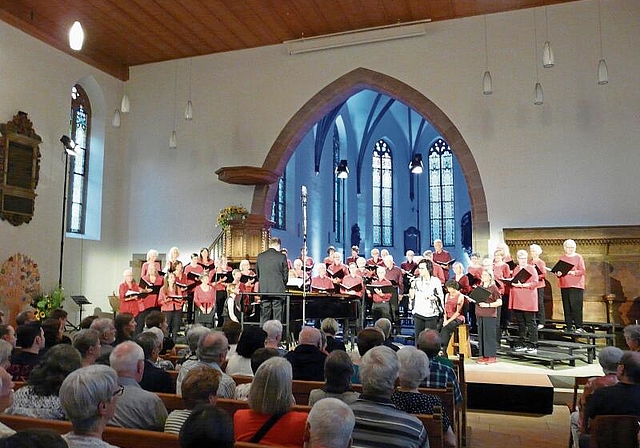 Die Singstimmen Baselland ganz in Rot gekleidet mit ihrem Dirigenten Jürg Siegrist und der Moderatorin Regi Sager.  Foto: A: Jegge