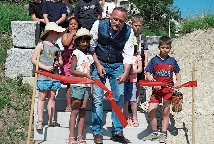Auf der Treppe des Thomas-Mosimann-Wegleins durchschneidet Gemeindepräsident Raymond Tanner das symbolträchtige Band inmitten der Schülerinnen und Schüler.