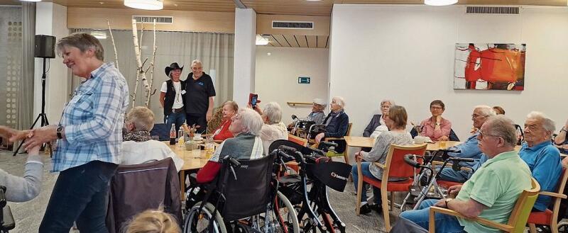 Die beiden Initiantinnen des Country-Nachmittags, links stehend Judith Wernli und mit Cowboyhut Martine Burget mit Bewohner Heinz Marending, Bewohnerinnen und Bewohner sowie Besucher schauen interessiert den Linedancers zu.