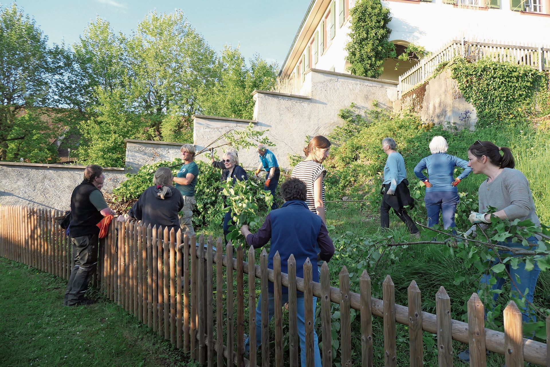 Eines der Igelhotels lehnt sich als grüner Asthaufen an die Mauer. Fotos: U. HandschinLetzte Äste schleppt unter anderem die Organisatorin Monika Handschin (r. aussen), während Kursleiter Michael Studer (3. v. l.) Anleitung gibt. 